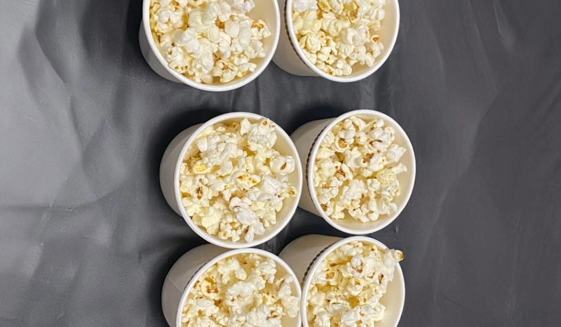 six small cups of popcorn on table covered with silver tablecloth