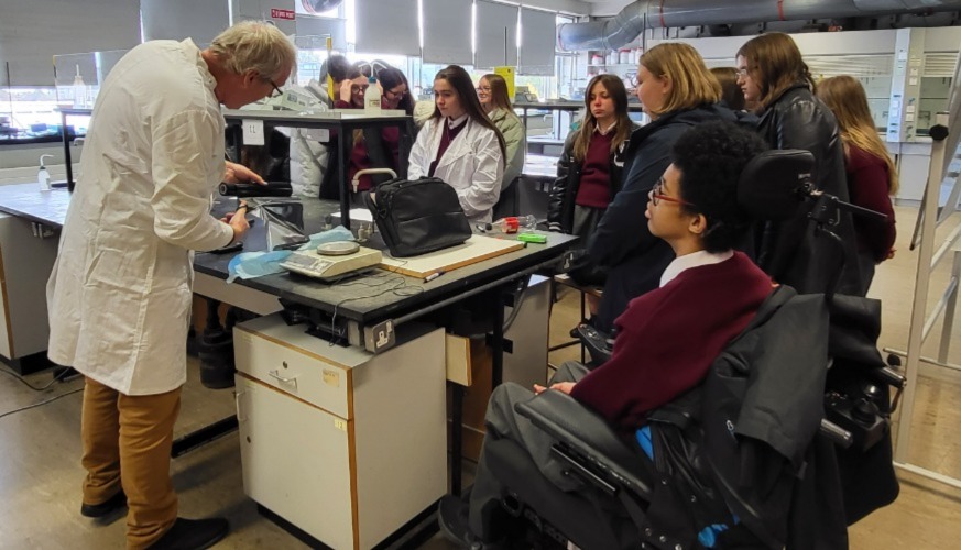 Group of secondary students, one in a wheelchair gathered around workstation in lab