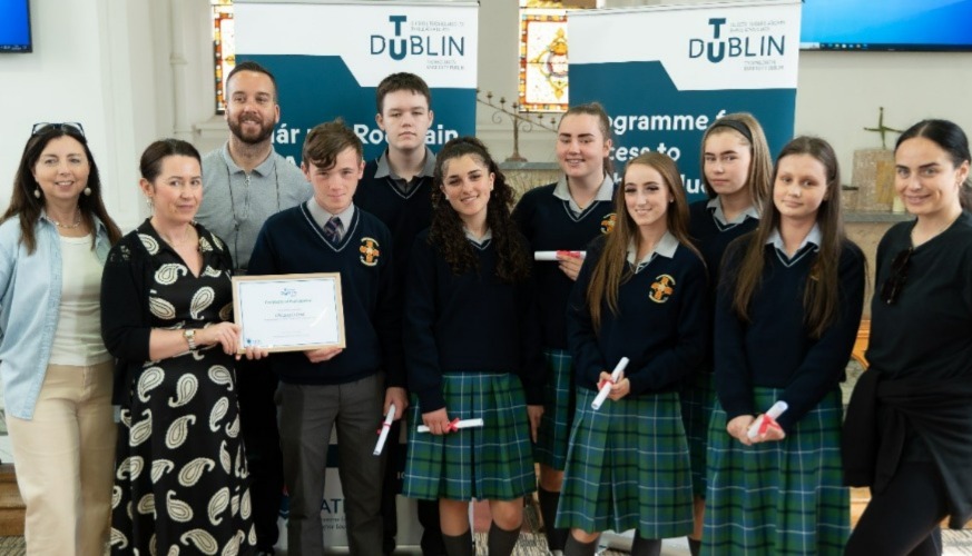 Group of TY students being presented with certificate standing in front of TU Dublin banners