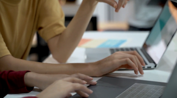 people's hands working on two laptops