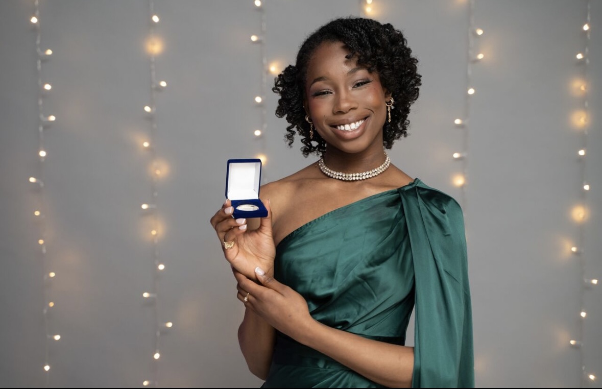 A smiling student in front of a gray background accented with warm, blurred string lights.