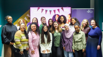 A group of students and teachers pose in front of a screen
