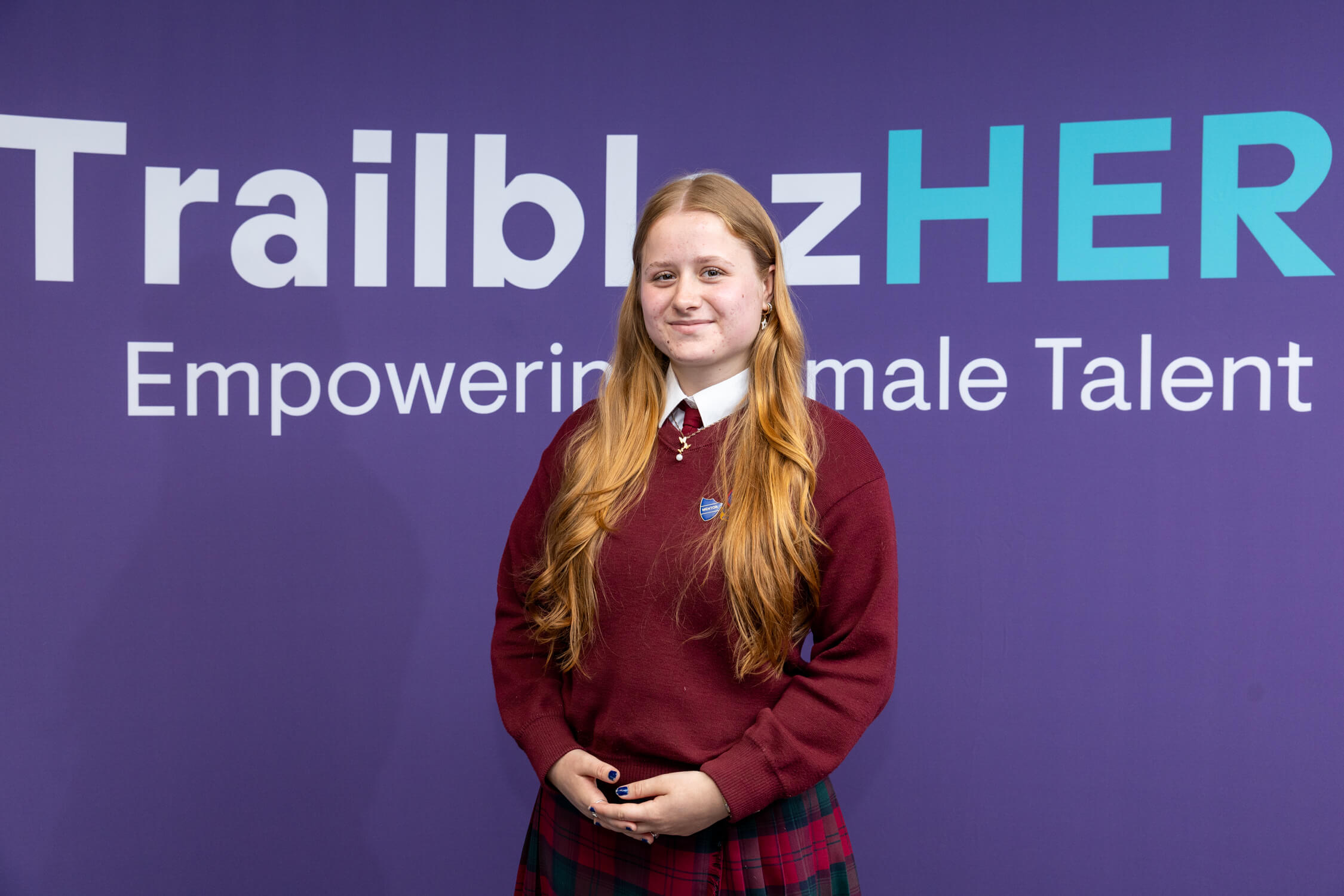 A young woman stands in front of a purple booth with TrailblazHER logo