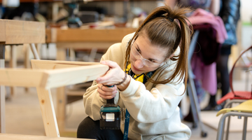 Image for A young women uses a drill on a wooden frame