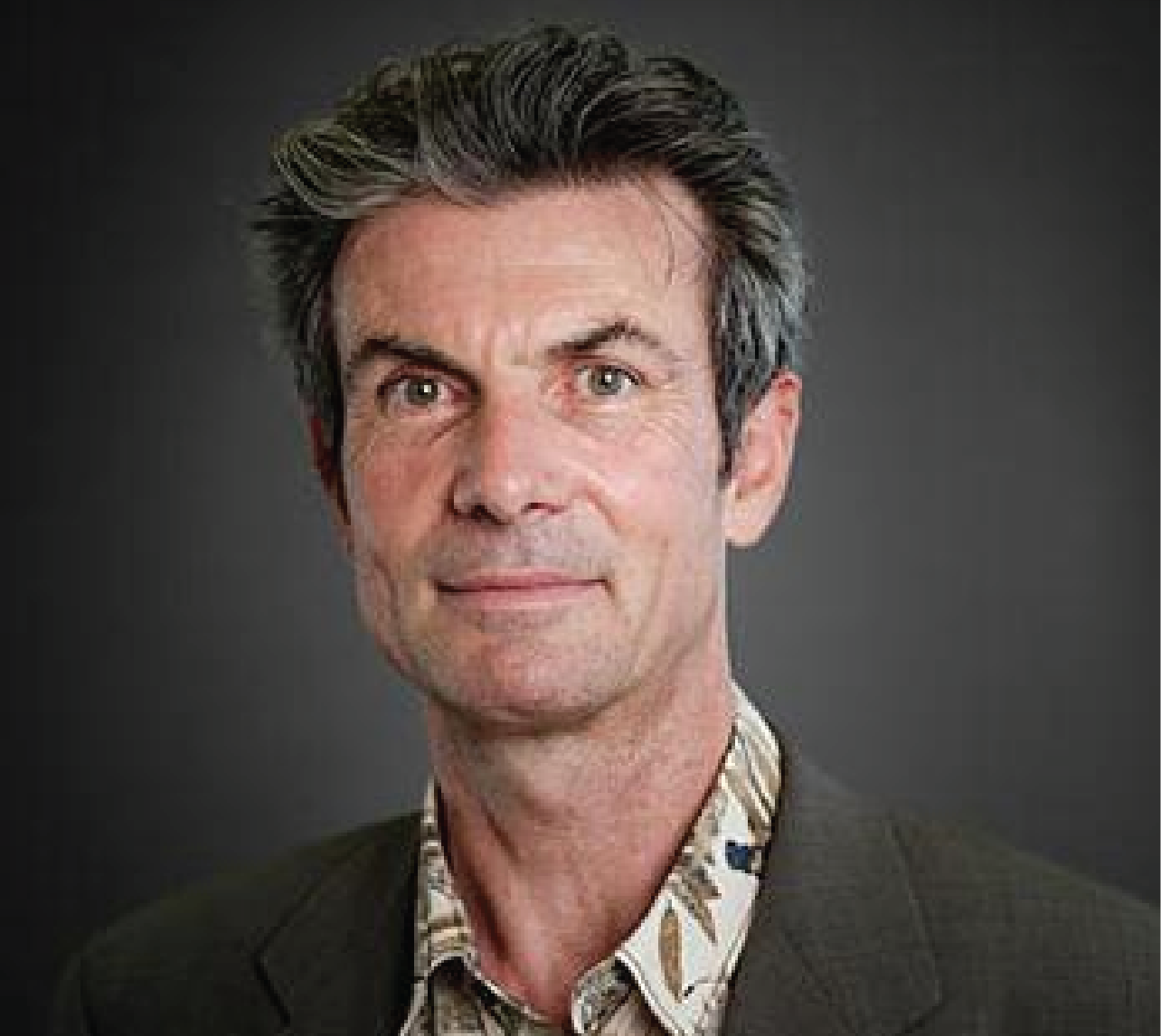 photo of white man with black grey hair wearing blazer and patterned shirt