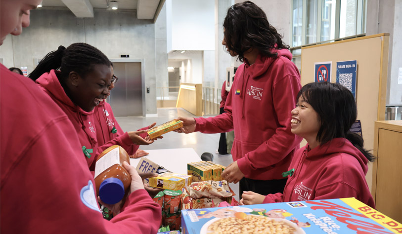 students in fuchsia pink college hoodies standing behind a table of pantry food giving out food