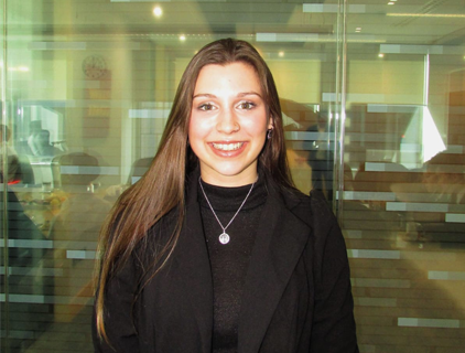profile photo of smiling young white woman with long dark hair standing in front of a glass room