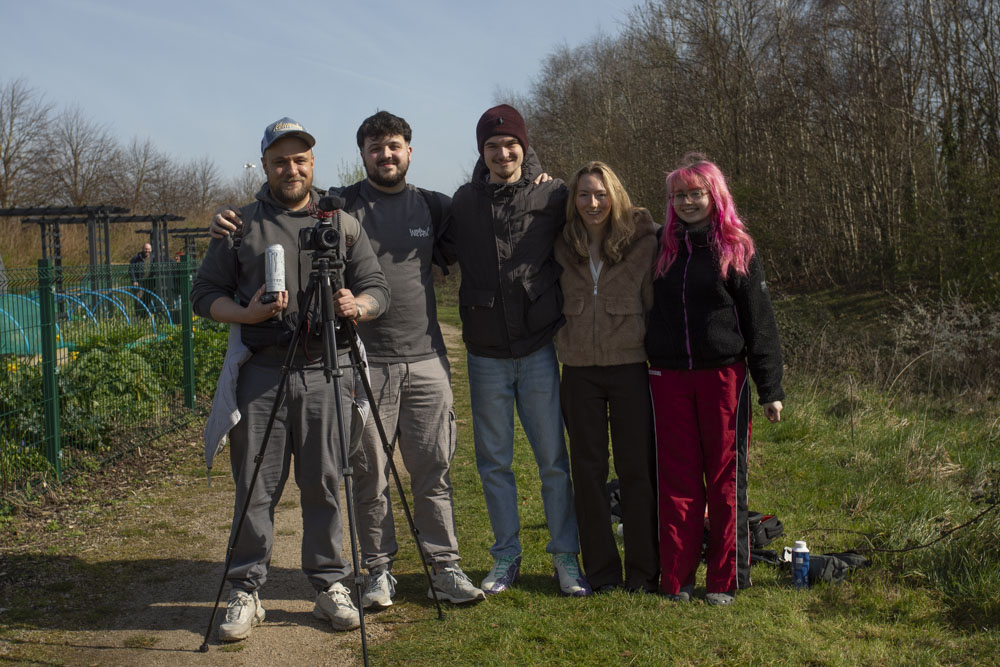 Four students standing in an outdoor green space, one holding a camera.