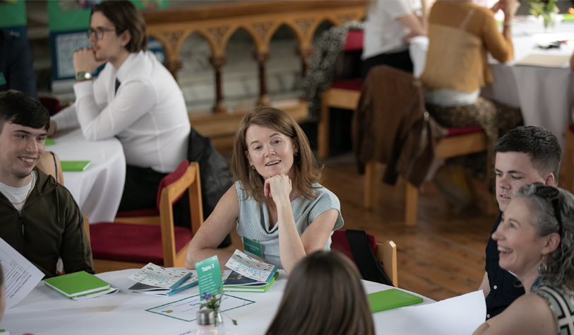 photo focus on women smiling with head gently leaning on chin, within a round seating at a round table