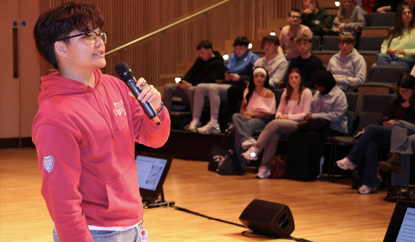 Male student in pink hoodie giving a talk to students in lecture