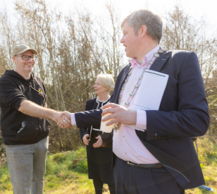 White man shakes another white man's hand. White woman looks on in.