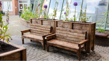 two wooden benches and two wooden planter boxes in a cobble locked courtyard of a building