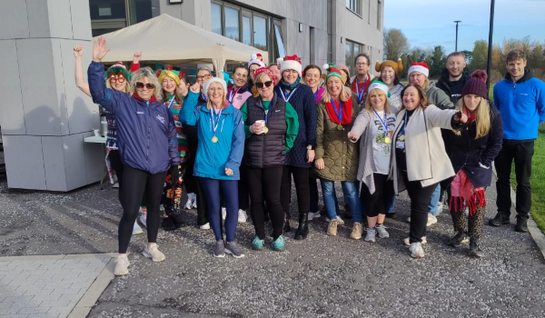 Group of around 30 people smile for camera against campus backdrop a grey building and blue sky