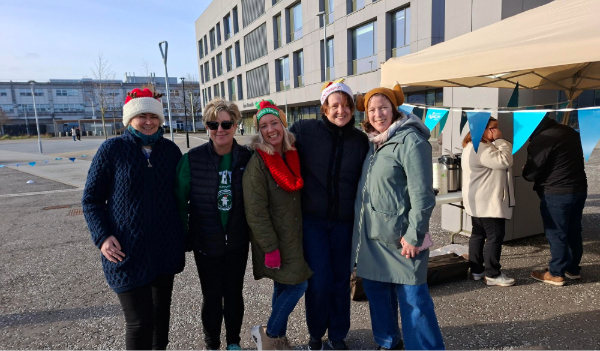 five females smile for camera some in festive hats against backdrop of campus buildings