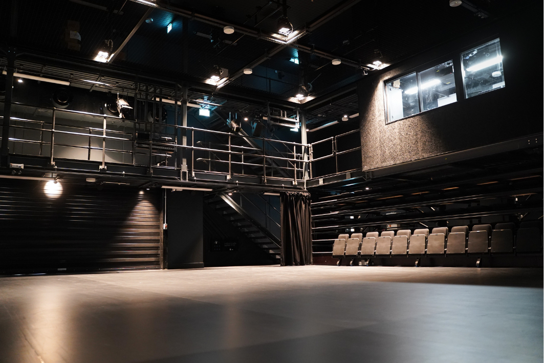 dark theatre with balcony surrounding it and a row of chairs behind the stage