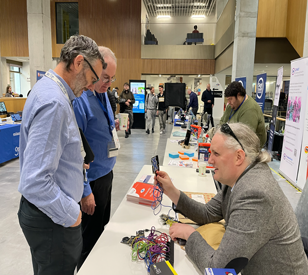 two people standing in hall talking to a man sitting down at exhibition stand