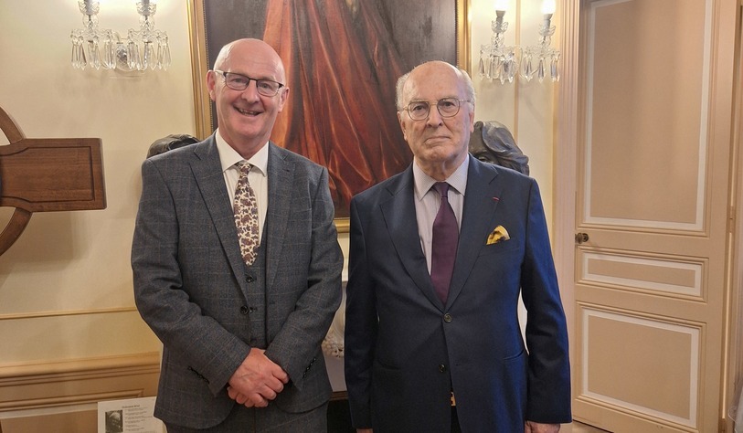 Two people post in front of a portrait of Princess Grace
