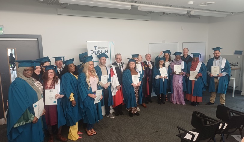 A group of people pose for a photo in front of a bronze tu dublin sign