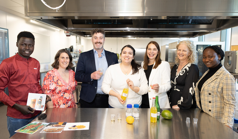 A group of people pose for a photo in a food development kitchen with liquids and beakers on a table