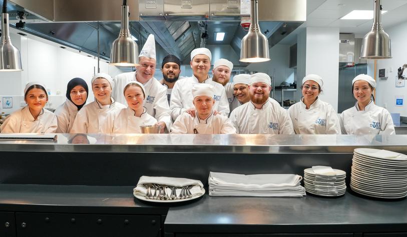 A group of student in chef whites pose for a photo in a kitchen
