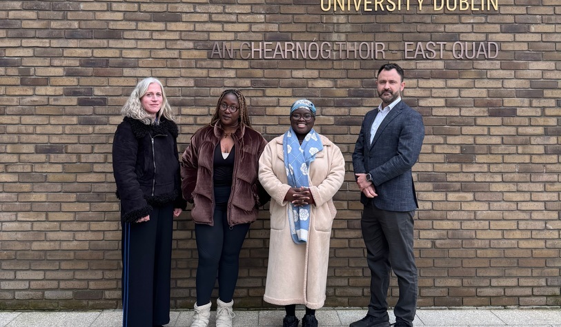 A group of people pose for a photo in front of a bronze tu dublin sign