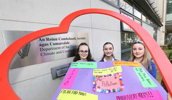 A photo of three young people holding a poster about air pollution