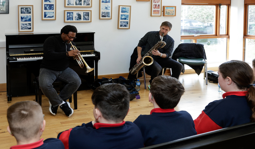 Two people play a trumpet and saxophone for an audience