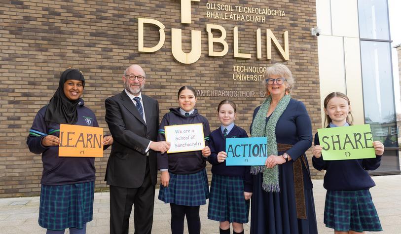 A group of people pose for a photo in front of a bronze tu dublin sign