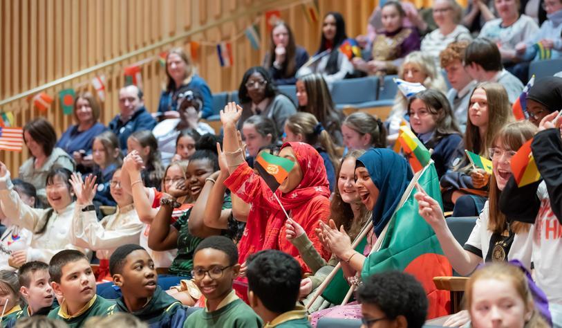 A group of pupils cheering and waving flags in an auditorium