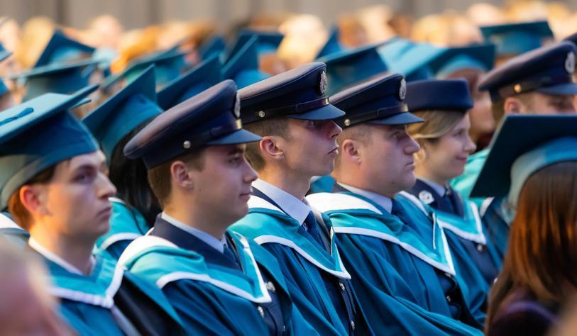 Graduates wearing blue and turquoise academic gowns and mortarboards sit together in rows during a Technological University Dublin graduation ceremony.