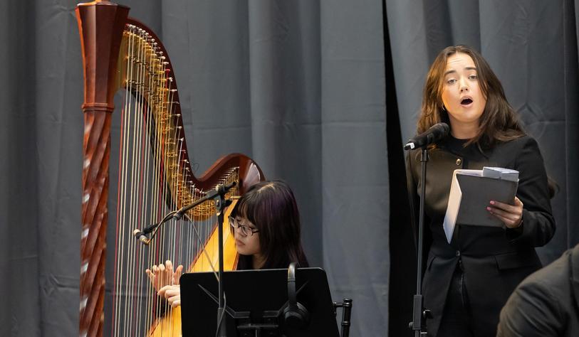 A harpist performs alongside a female vocalist during a TU Dublin graduation ceremony, providing live musical entertainment on stage.