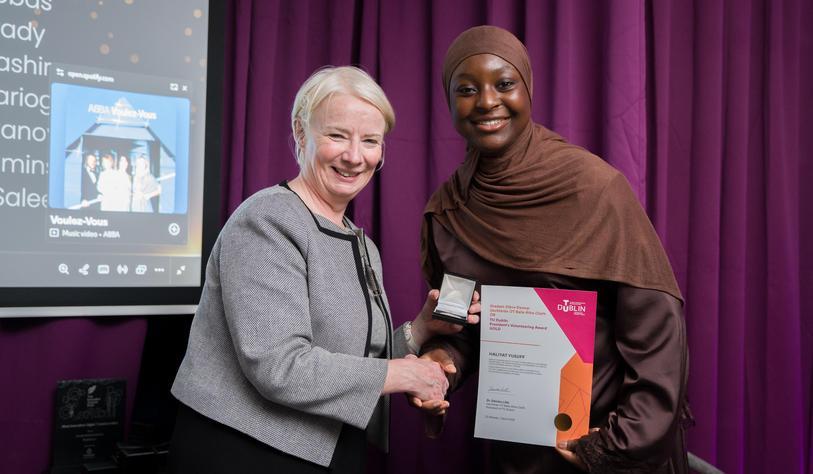 Two people shake hands and smile, with one person holding a certificate