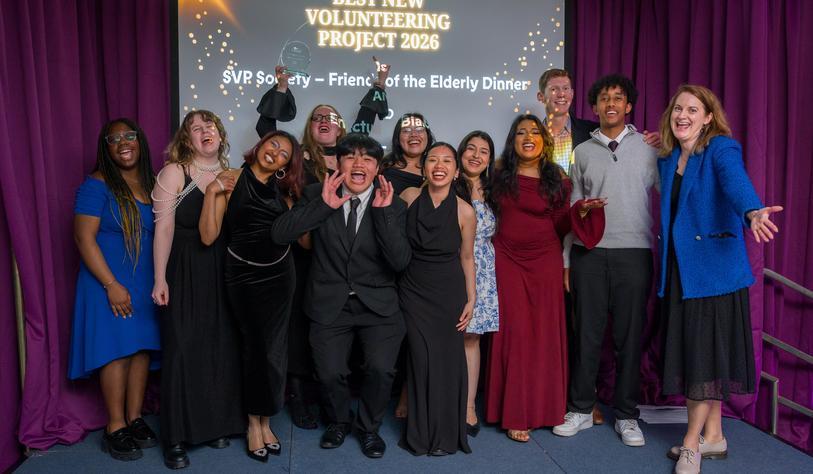 People pose and smile for a happy celebratory photo in front a banner that says best new volunteering society