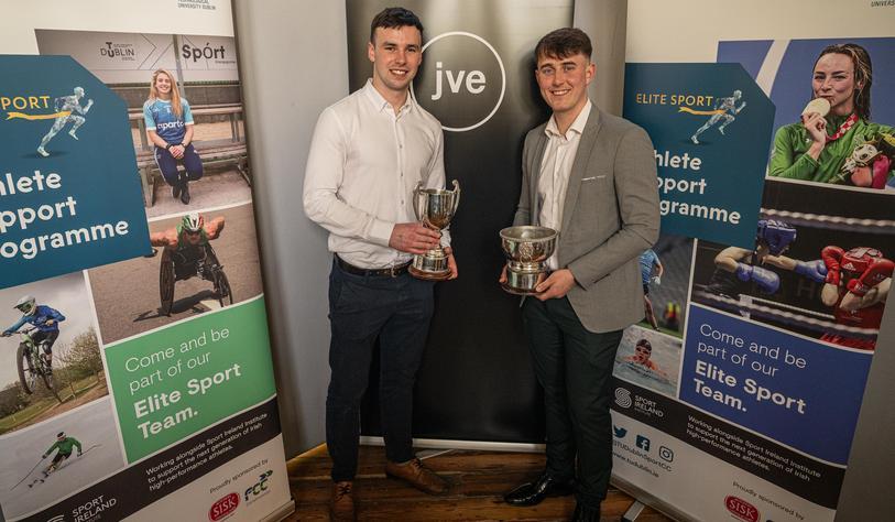 Two people smiling and holding trophies