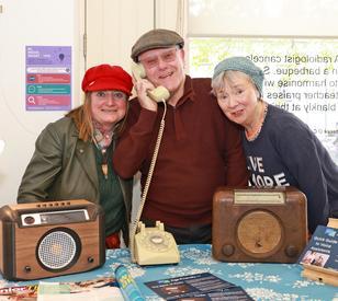 Three people post in front of two old fashioned radios and a telephone