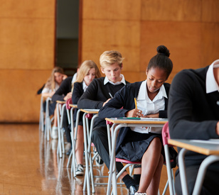 Teenage Students In Uniform Sitting Examination In School Hall