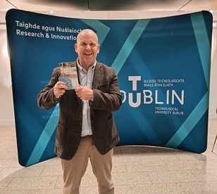 Image of Dr Keith Muprhy holding an award in front of a banner of the TU Dublin logo
