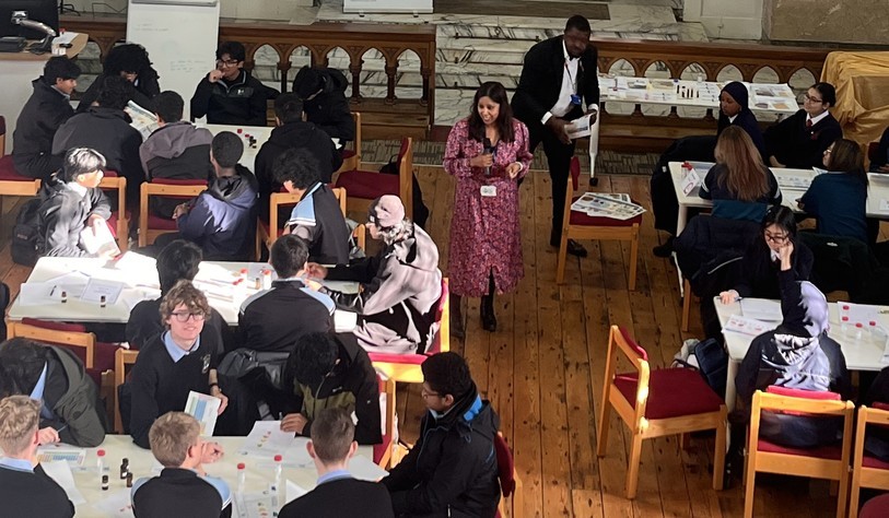tudents working collaboratively in small groups at tables during a Future of Food workshop, with a presenter addressing participants.