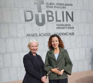 Two people stand in front of a TU Dublin logo
