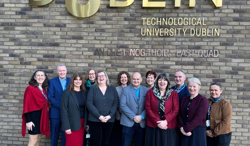 A photo of people standing in front of a bronze tu dublin logo