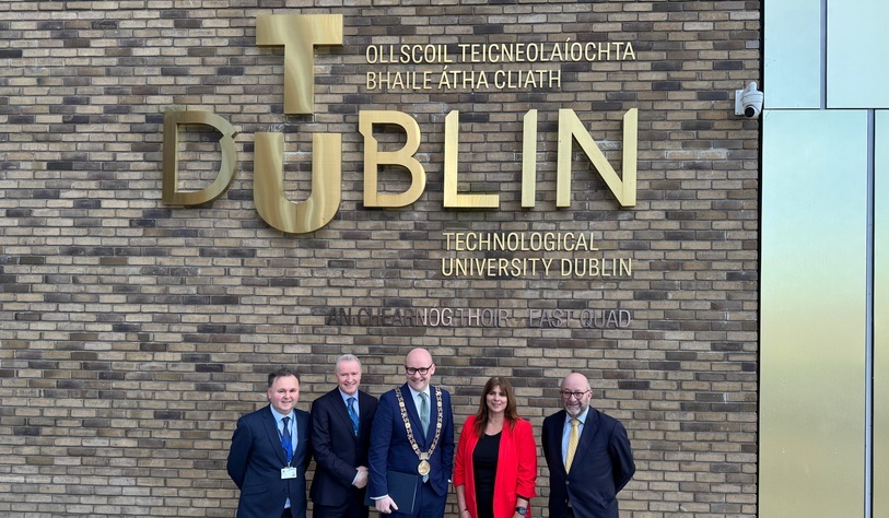 A group of people pose for a photo in front of a bronze tu dublin sign