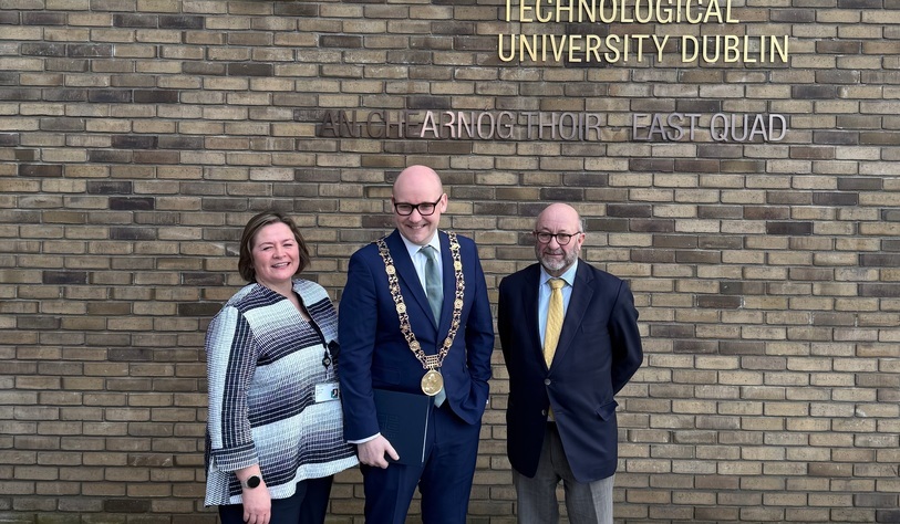 A photo of people standing in front of a bronze tu dublin logo