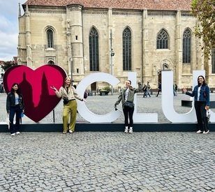 Four students pose beside a large “I ♥ CUL” sign in a cobblestoned European square, with a historic Gothic church visible in the background.