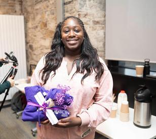 A photo of a student holder a purple jumper and flowers