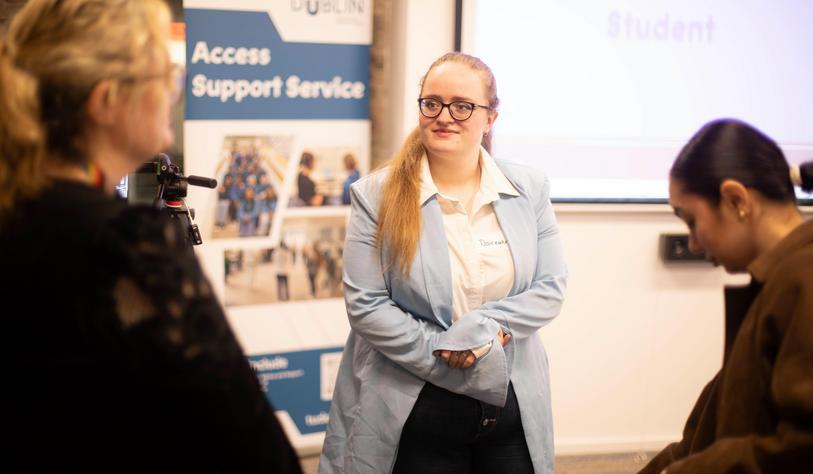 A young person in a blue jacket posed in front of a banner that says Access Support Service