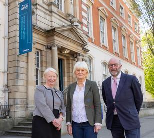 Three people pose in front of a neo-classical building with a banner that says TU Dublin and trees in the background