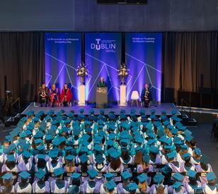 Overview of the Technological University Dublin graduation ceremony, with rows of graduates in turquoise and blue academic gowns seated in front of the stage.