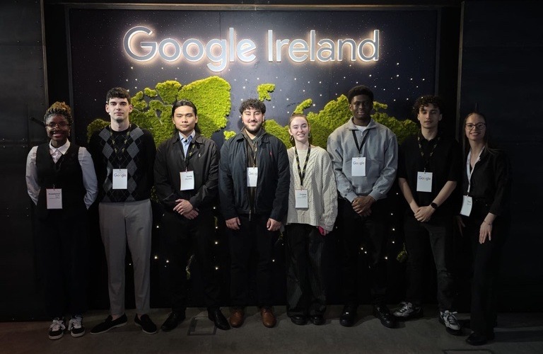 Seven people stand smiling in front of a 