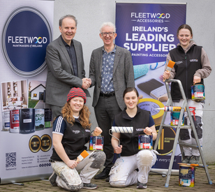 Two men are shaking hands in front of Fleetwood banners, flanked by three smiling women holding paint supplies, conveying a collaborative tone.