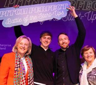 Four people, smiling and standing together, hold up a sign reading 
